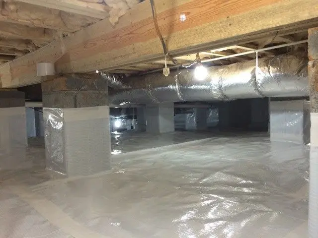 An encapsulated crawl space: white vapor barrier over the ground and up the piers, with foil-wrapped ductwork under the floor joists