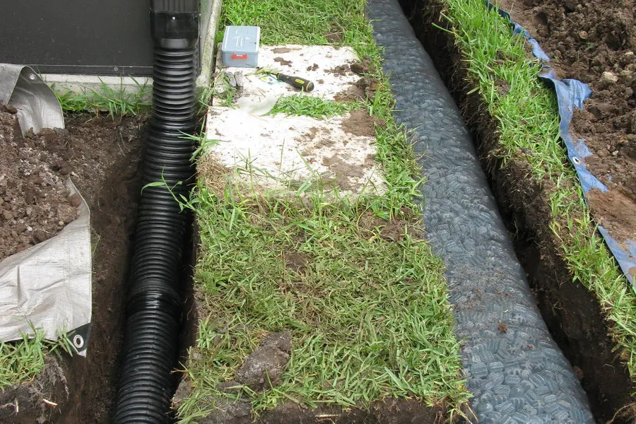 French drain trench with gravel and pipe being installed along a home