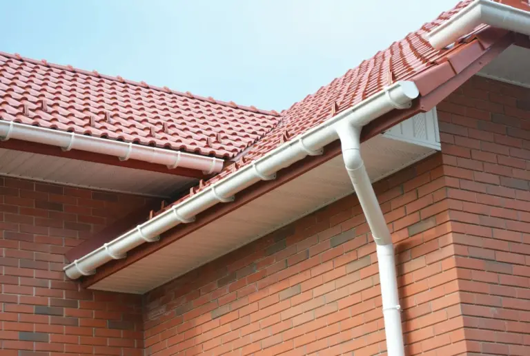 A white gutter and downspout on a red brick house with a tile roof