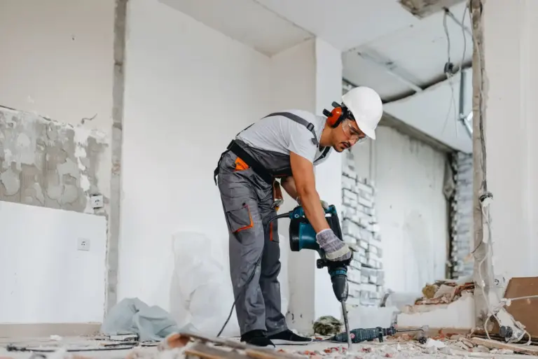 A worker in a hard hat and ear defenders drilling into a concrete floor during a renovation