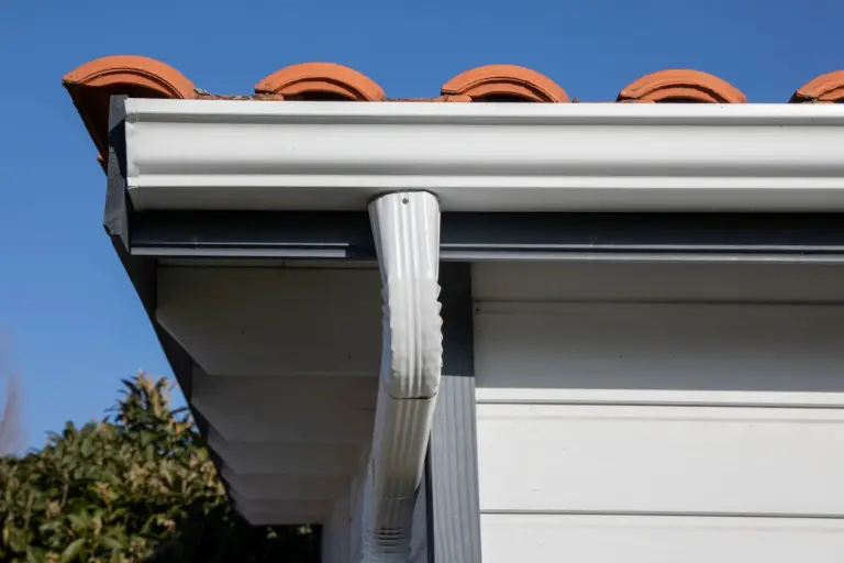 A white gutter and downspout under a terracotta tile roof, seen from below