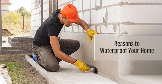 A worker in an orange hard hat brushes waterproof coating onto a block foundation wall, beside the words Reasons to Waterproof Your Home