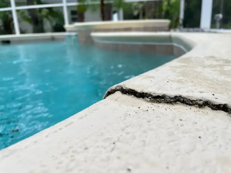 A cracked, uneven concrete pool deck at the edge of a swimming pool